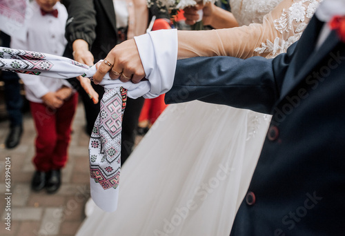 The bride and groom stand at the ceremony with an embroidered towel tied in a knot on their hands. Wedding photography, Ukrainian tradition, ritual, portrait, lifestyle.