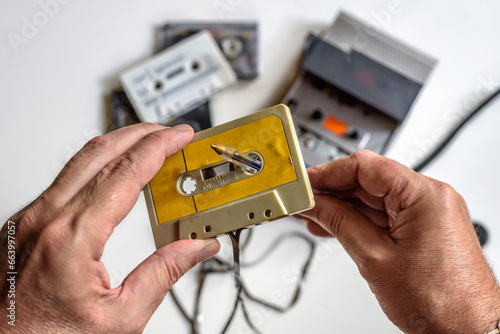 Rebobinando manualmente una cinta de casete con la ayuda de un boli, reproductor de casetes y varias cintas sobre fondo blanco. photo