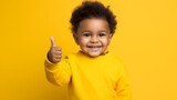 A cute black toddler showing a thumbs up on yellow background