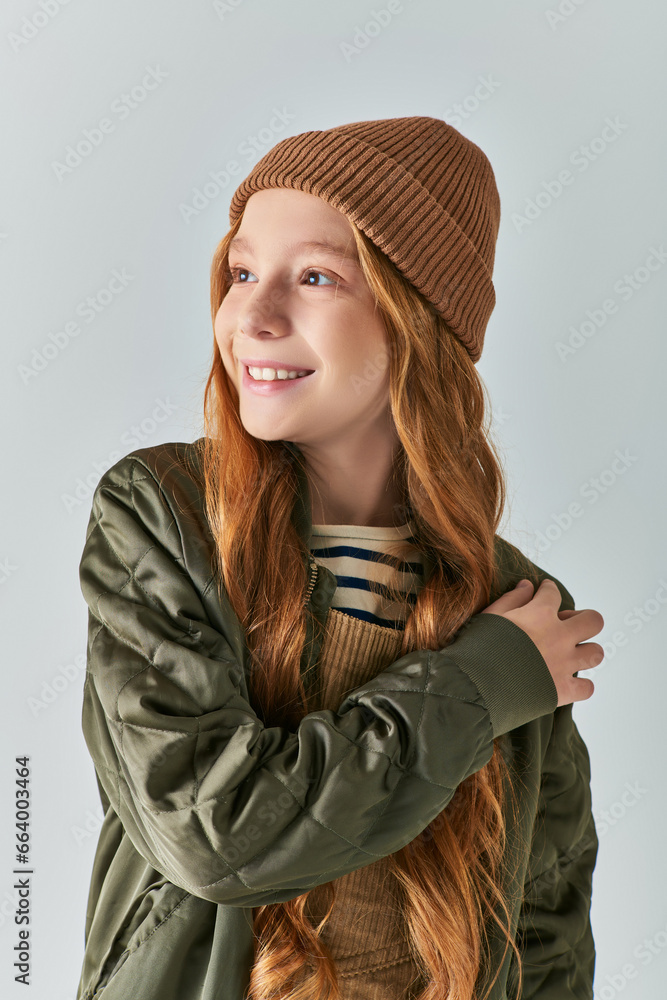 winter fashion, dreamy girl in knitted hat and outerwear looking away on grey backdrop winter fashion, dreamy girl in knitted hat and outerwear looking away on grey backdrop