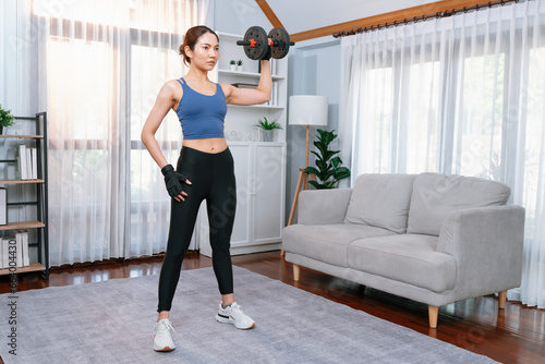 Vigorous energetic woman doing dumbbell weight lifting exercise at home. Young athletic asian woman strength and endurance training session as home workout routine.