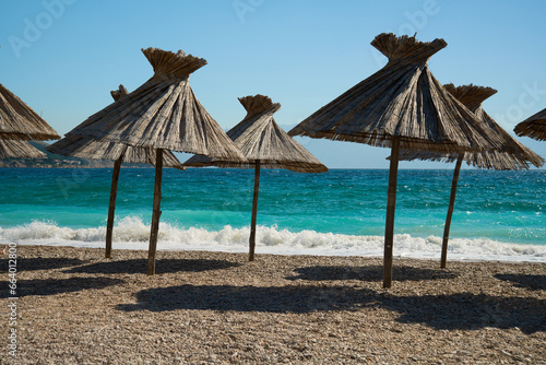 Fototapeta Naklejka Na Ścianę i Meble -  A beautiful beach with small golden pebbles and straw umbrellas on the turquoise seashore.