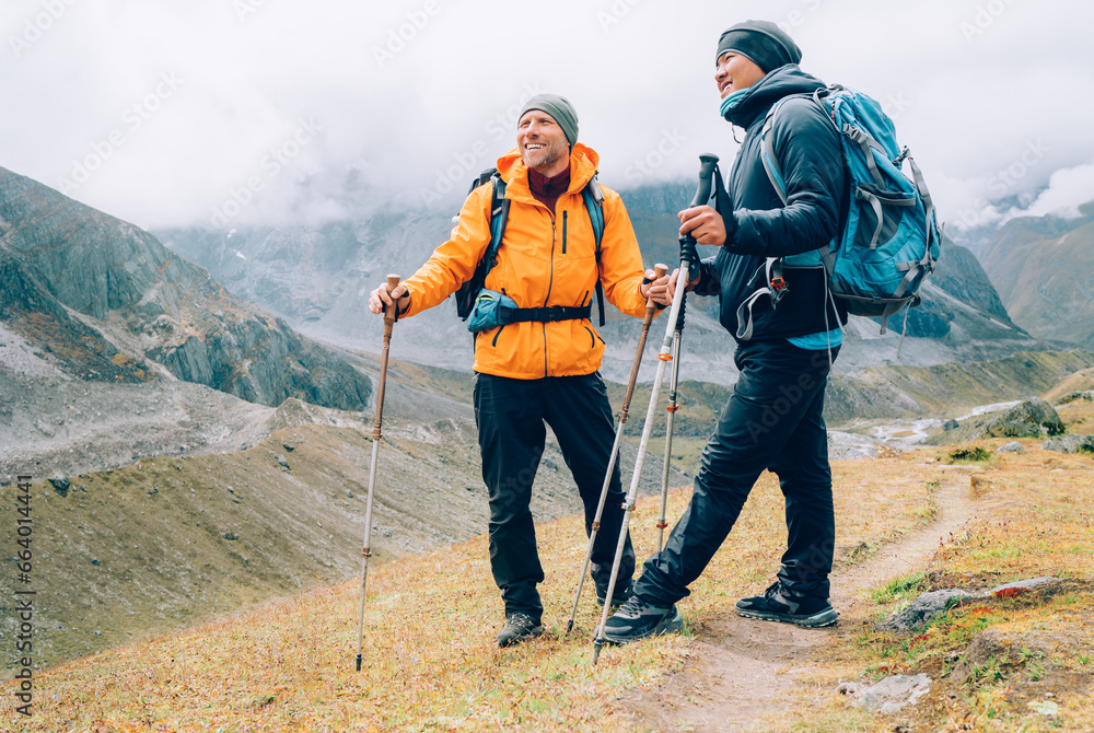Caucasian and Sherpa men with backpacks with trekking poles together smiling enjoying Mera peak climbing acclimatization walk  Makalu Barun Park route. Backpackers enjoying beautiful valley view - obrazy, fototapety, plakaty 