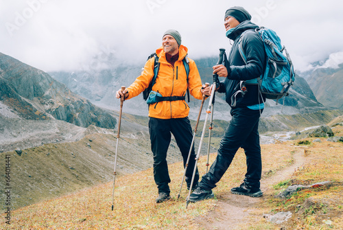 Caucasian and Sherpa men with backpacks with trekking poles together smiling enjoying Mera peak climbing acclimatization walk  Makalu Barun Park route. Backpackers enjoying beautiful valley view photo