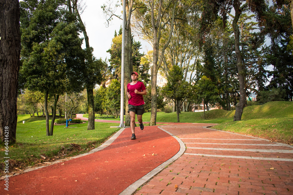 Man wearing red cap, running in park at sunset