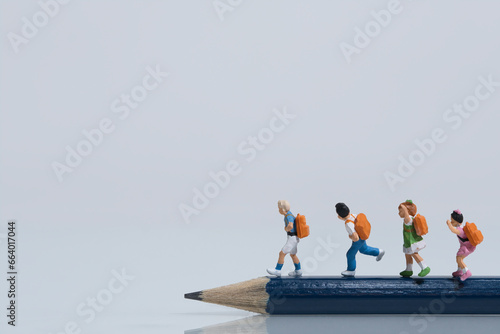 Schoolchildren with schoolbags walk on a sharp pencil, miniature figures scene, white background, copy space