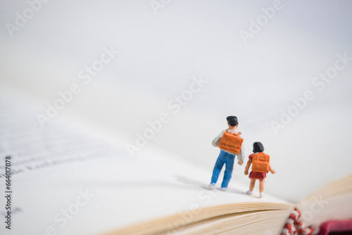 Schoolchildren with schoolbags walk on an open book, miniature figures scene photo