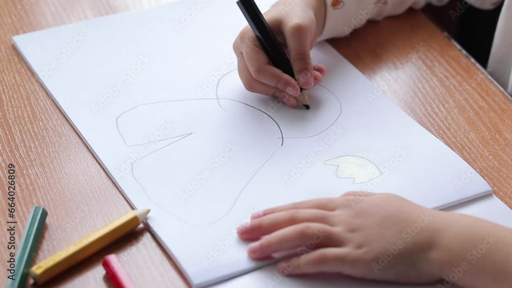 A child draws with colored pencils in an album. Children's creativity, learning in kindergarten, school or at home. Child's hand with a pencil close-up, selective focus. Girl draws a picture A child draws with colored pencils in an album. Children's creativity, learning in kindergarten, school or at home. Child's hand with a pencil close-up, selective focus. Girl draws a picture