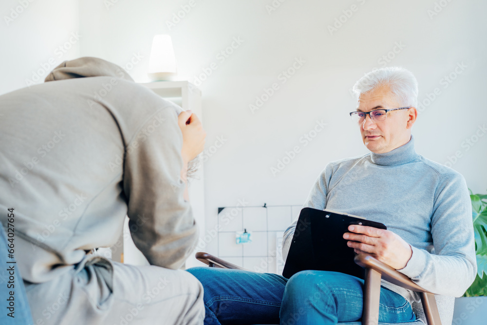 Obraz premium Professional psychotherapy. Male psychologist having session with male patient at mental health clinic, Taking Notes During Appointment In Office. Psychological help service. Treatment of depression