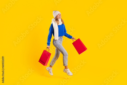 Big seasonal sales. Lady shopaholic holding shopping bags and running in mid-air, wearing sweater, scarf and hat