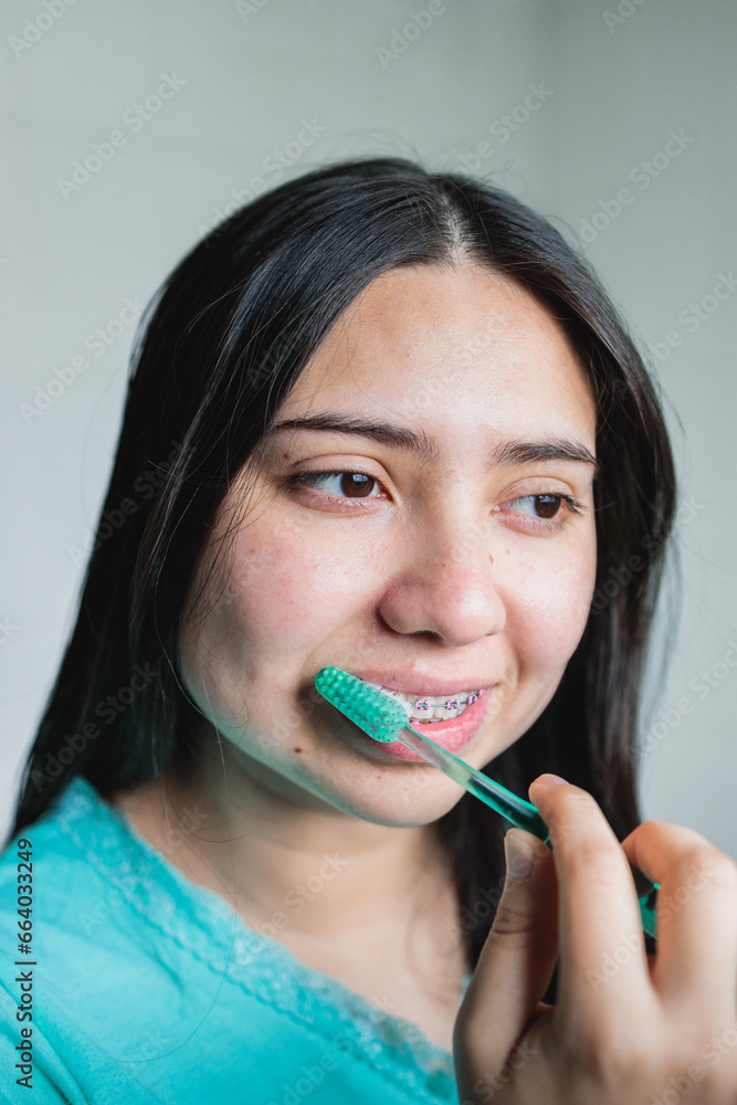 Close up of smiling young woman with braces brushing her teeth in the bathroom. Oral Hygiene routine Close up of smiling young woman with braces brushing her teeth in the bathroom. Oral Hygiene routine