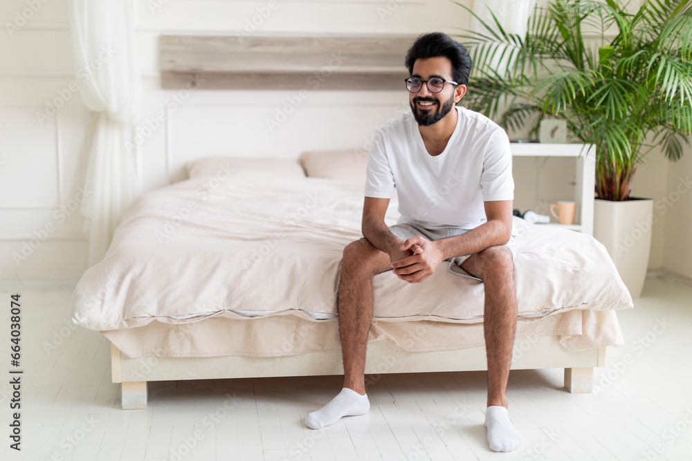 Portrait Of Happy Young Indian Man Sitting On Bed In Bedroom Portrait Of Happy Young Indian Man Sitting On Bed In Bedroom
