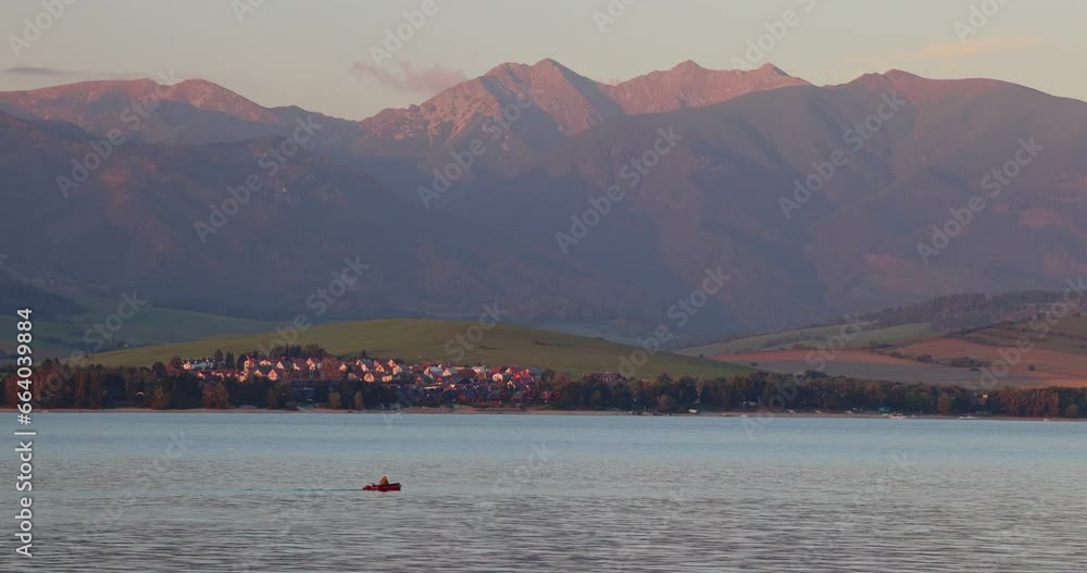 Landscape with mountain and lake with a small boat floating at sunset. The Liptovska Mara lake with Western Tatras mountain in Slovakia. Europe. Landscape with mountain and lake with a small boat floating at sunset. The Liptovska Mara lake with Western Tatras mountain in Slovakia. Europe.