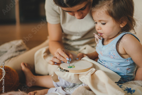 Foto Portrait of young mother teaching her cute little baby daughter to embroidery with embroider frame sitting on the floor at home
