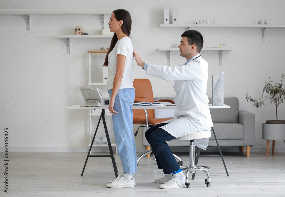Male doctor checking posture of young woman in clinic - obrazy, fototapety, plakaty 
