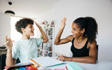 Cheerful woman helping daughter doing homework. Mother and daughter shaking hands while doing school homework in living room.