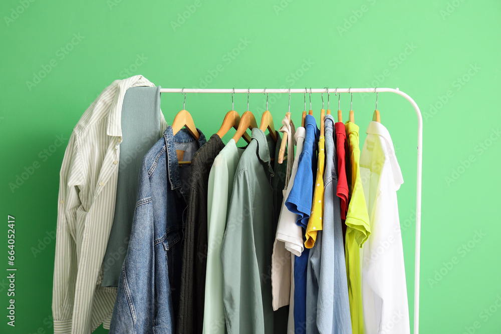 Stylish clothes hanging on rack against green wall, closeup