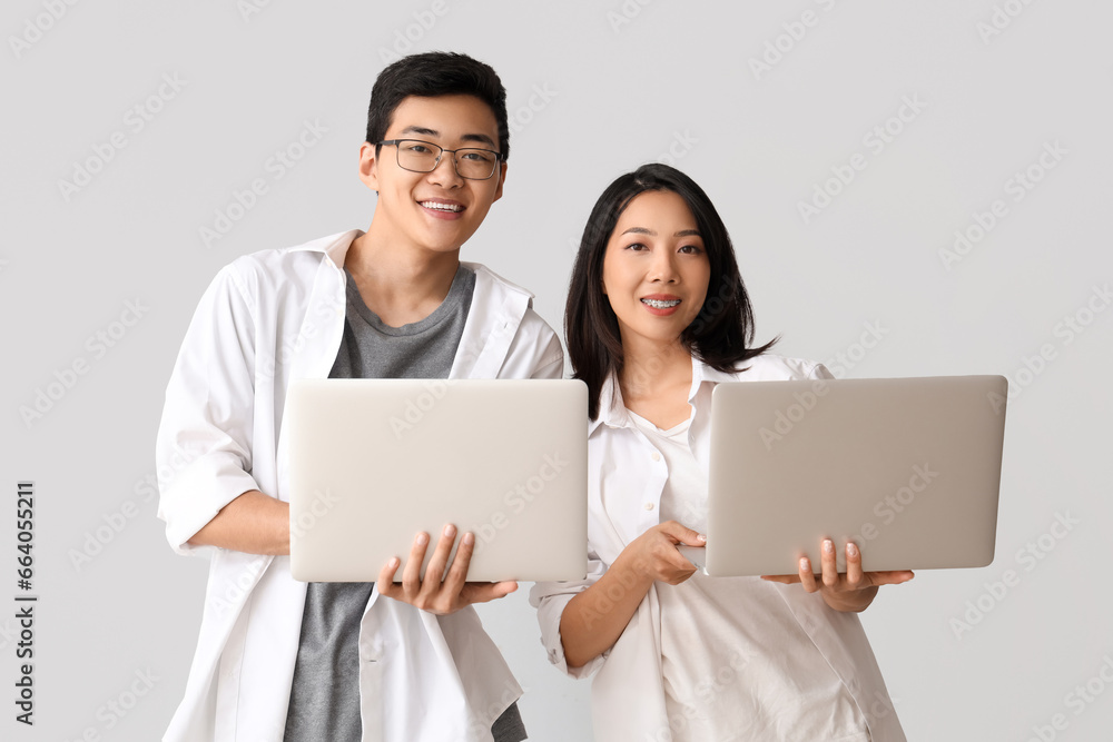 Young Asian friends with laptops on light background Young Asian friends with laptops on light background