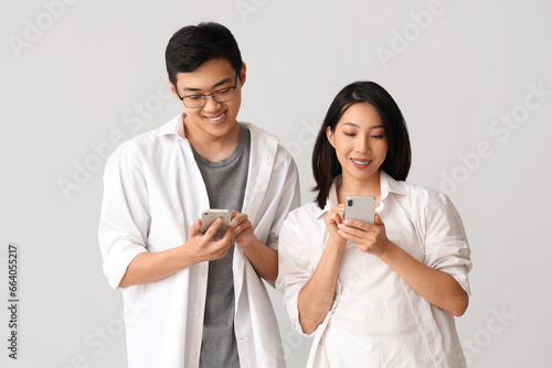 Young Asian friends using mobile phones on light background