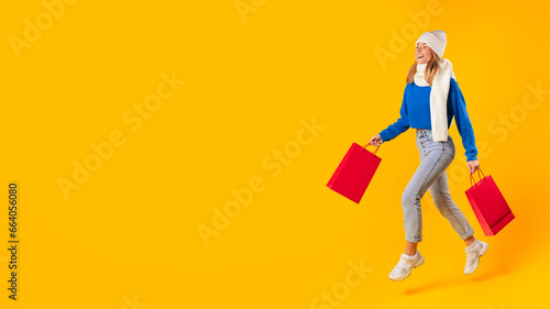 Winter sales and shopping. Excited lady consumer walking and looking at copy space, holding colorful bags