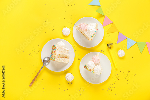 Birthday decorations and plates with pieces of yummy cake on yellow background