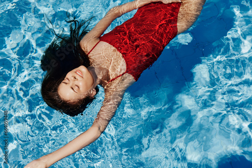 Young woman in the pool in a red swimsuit with a beautiful smile lying on the water and swimming in the sun swimming in the pool, the concept of relaxing on vacation.