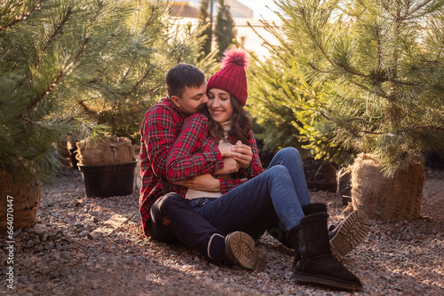 Close-up portraits of young couple in red checkered shirts sitting among Christmas tree seedlings © farmuty
