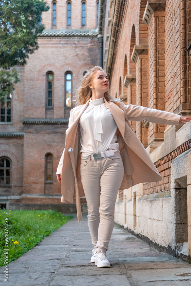 Full-length portrait of young woman in light pastel colors outfit near red brick building. Vertical frame.