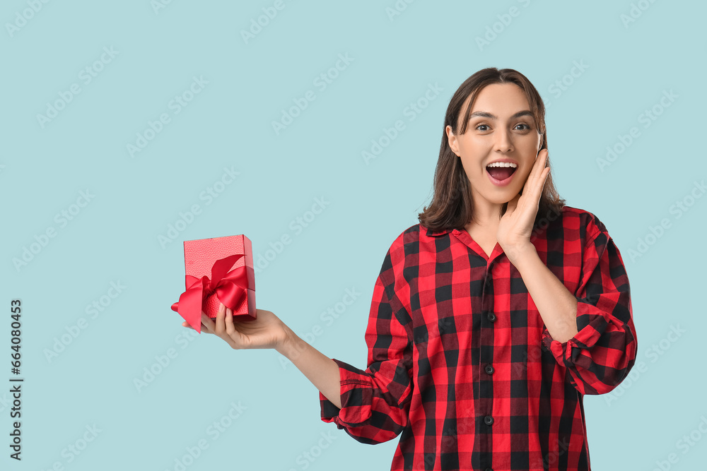 Beautiful young woman in pajamas with gift box on blue background Beautiful young woman in pajamas with gift box on blue background