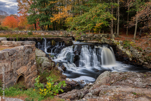 Small waterfall over stone dam in autumn forest with colorful foliage