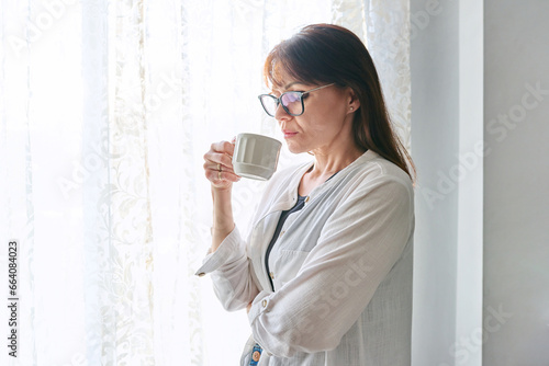 Serious middle-aged woman looking out window, with cup in hands photo