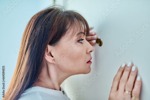 Serious middle-aged woman looking through peephole on front door photo