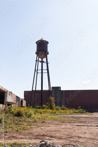 A beautiful water tower is set around an abandoned area. This rusty metal structure stands tall against a blue sky.