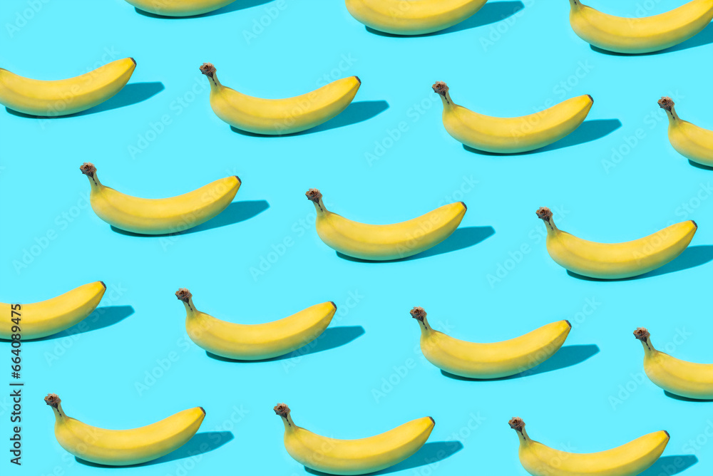 Trendy Summer food pattern made with yellow bananas on bright light blue background. Minimal summer concept.