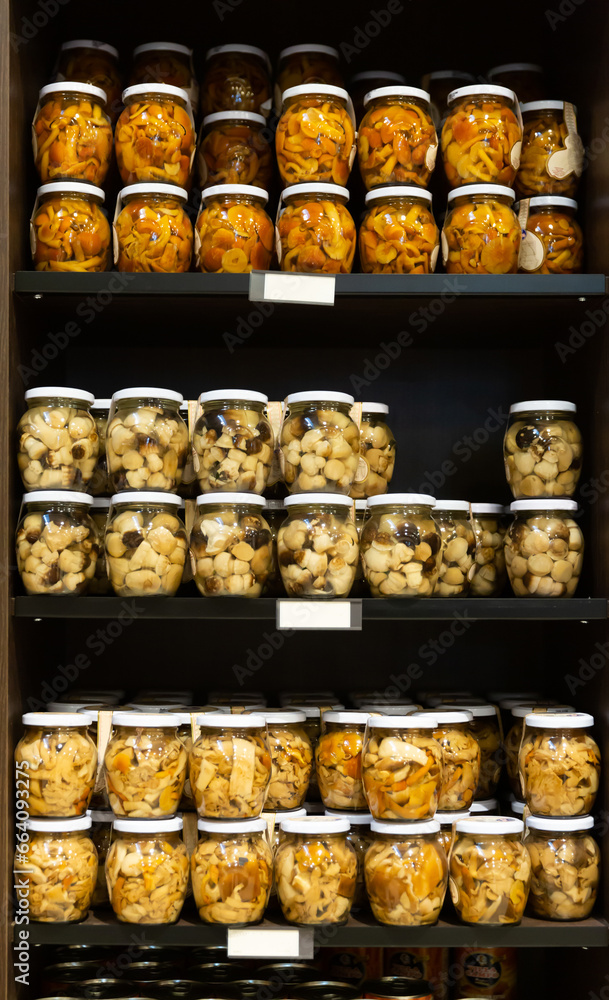 Closed glass jars with various pickled mushrooms for sale on shelf in store