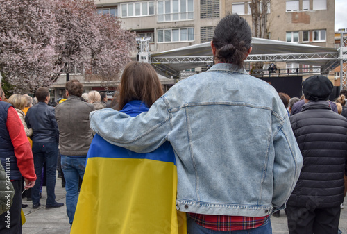 A girl draped in a Ukrainian flag at a protest against the war in Ukraine. A young couple supports Ukraine.