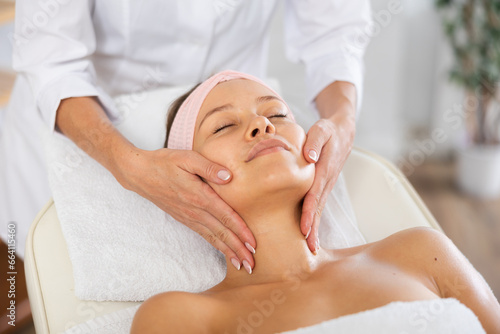 Portrait of young female client getting soothing and relaxing facial massage to help relieve stresses in spa center ..