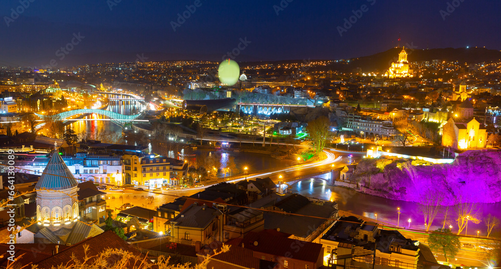 Night spring cityscape of historical area of Tbilisi illuminated by colorful lights with view of modern bow-shaped bridge across Mtkvari River, Georgia
