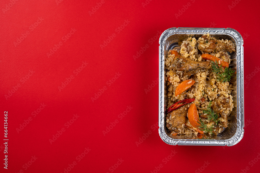 Boiled Rice with Chicken and Carrots in a Disposable Foil Box on a Red Background
