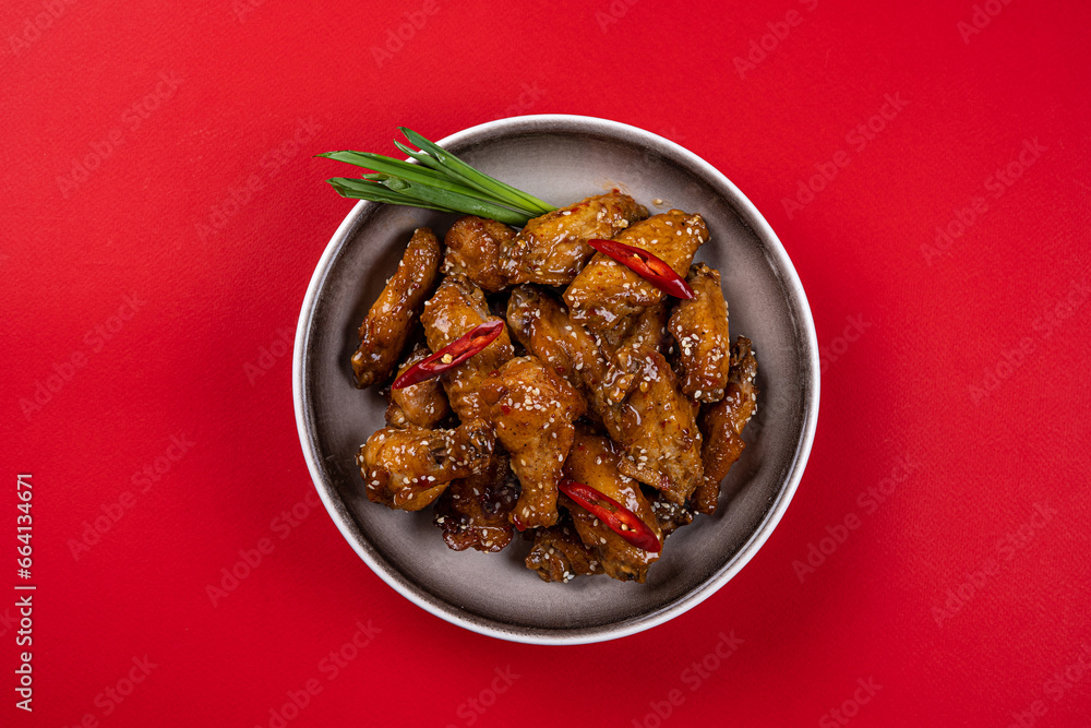 Chicken Drumsticks and Wings in Spicy Teriyaki Sauce with Sesame Seeds on a Gray Plate on a Red Background Chicken Drumsticks and Wings in Spicy Teriyaki Sauce with Sesame Seeds on a Gray Plate on a Red Background