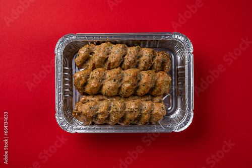 Lule Kebab Dish for Delivery in Foil Packaging Box on a Red Background photo