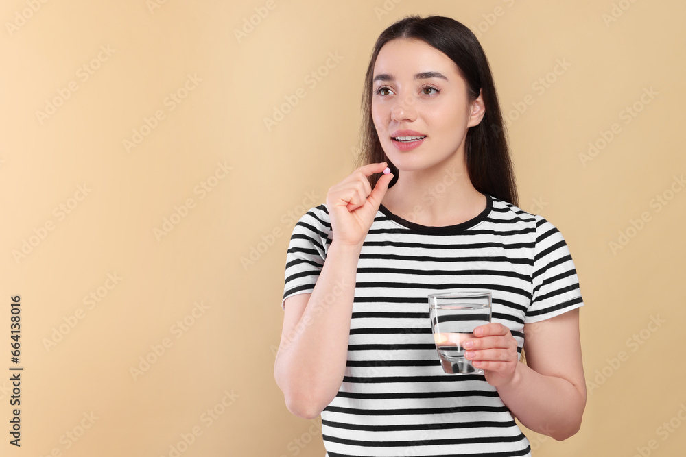 Happy woman with glass of water taking pill on beige background, space for text Happy woman with glass of water taking pill on beige background, space for text
