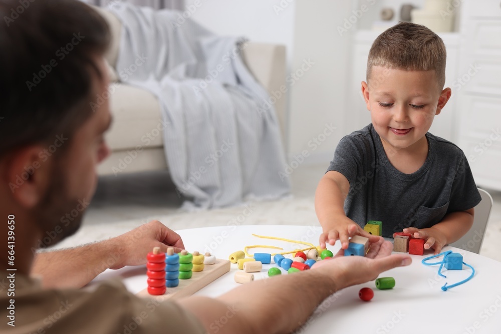 Fototapeta premium Motor skills development. Father and his son playing with wooden pieces at table indoors