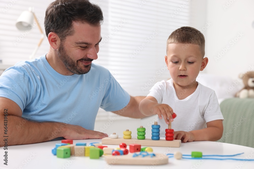 Motor skills development. Father and his son playing with stacking and counting game at table indoors Motor skills development. Father and his son playing with stacking and counting game at table indoors