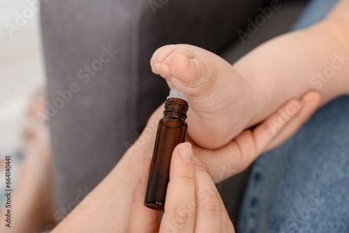 Mother applying essential oil from roller bottle onto her baby s heel on blurred background  closeup