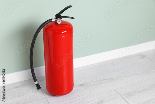 Red fire extinguisher near light green wall. Space for text © New Africa