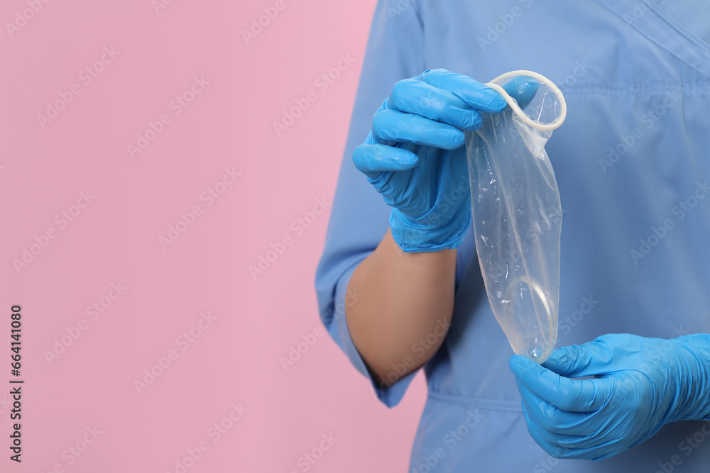 Fototapeta premium Doctor with unrolled female condom on pink background, closeup. Space for text