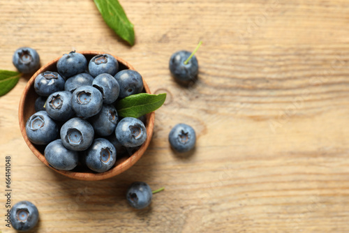 Bowl of tasty fresh blueberries and green leaves on wooden table, flat lay. Space for text
