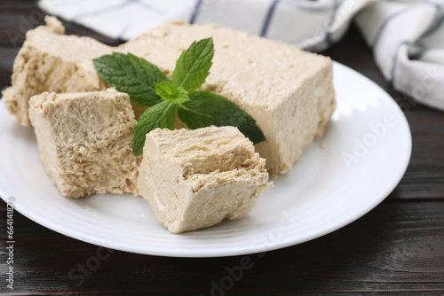 Plate with pieces of tasty halva and mint on wooden table, closeup