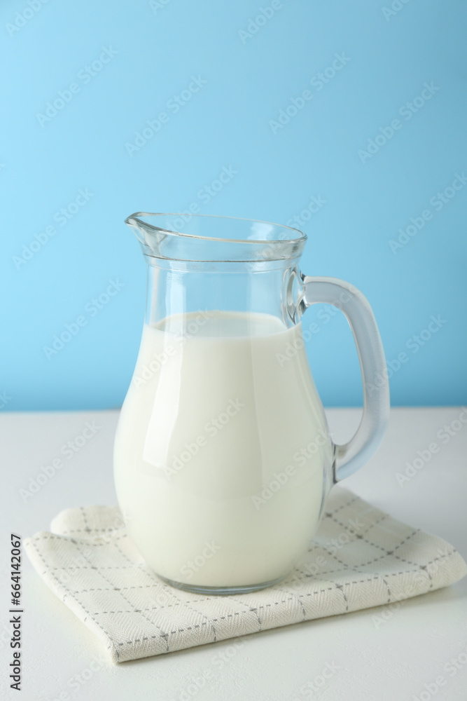 One jug of fresh milk on white table against light blue background One jug of fresh milk on white table against light blue background